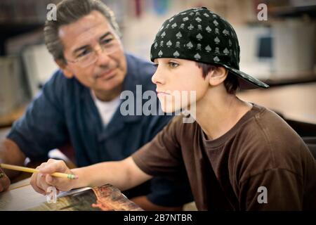 Teenager, der mit einem erwachsenen männlichen Lehrer in der Klasse sitzt. Stockfoto