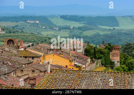 Dächer der Altstadt von San Gimignano, das Haupttor Porta San Giovanni und Bastione San Francesco mit toskanischen Landschaft im Hintergrund, Italien. Stockfoto