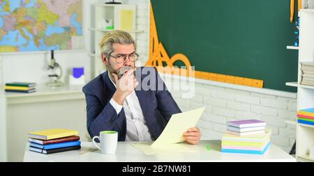 College High School. Die Abschlussprüfung kann mündlich oder praktisch erfolgen. Lehrer erklärt Theorie. Vorbereitung auf den Test. Lehrer bärtiger Mann Hintergrund des Schwarzen Bretts. Lehrerarbeit. Dozent im Klassenzimmer. Stockfoto