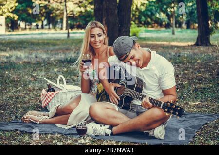 Junge Paare genießen ihre Zeit und haben ein romantisches Picknick im Park. Gitarre und Gesang spielen. Romantik, Dating und Liebeskonzept. Stockfoto