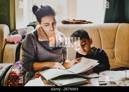 Elternhilfe bei Hausaufgaben. Authentisches Foto der jungen Mutter, die ihrem kleinen Jungen bei der Hausaufgabe hilft Stockfoto