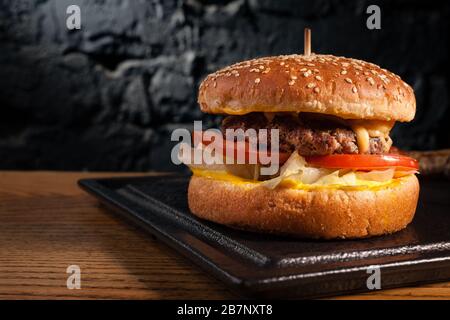 Appetitlicher Burger auf Holztisch und Seitenansicht. Vor dem Hintergrund einer schönen, schwarzen Wand. Leerzeichen. Stockfoto