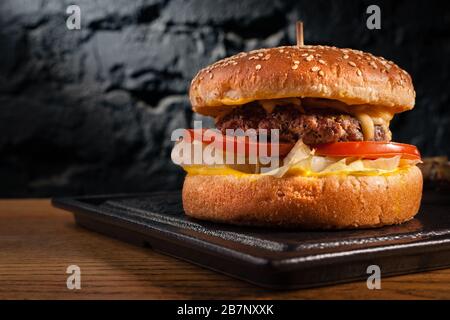 Appetitlicher Burger auf Holztisch und Seitenansicht. Vor dem Hintergrund einer schönen, schwarzen Wand. Leerzeichen. Stockfoto