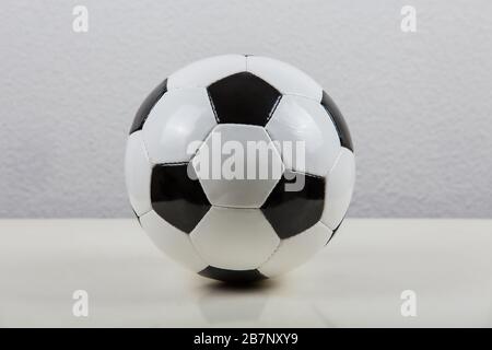 Klassischer Fußball-Ball auf dem Tisch, schwarz-weiß typisches Sechskant, isoliert auf grauem Hintergrund. Echtes, traditionelles Fußballsymbol. Stockfoto