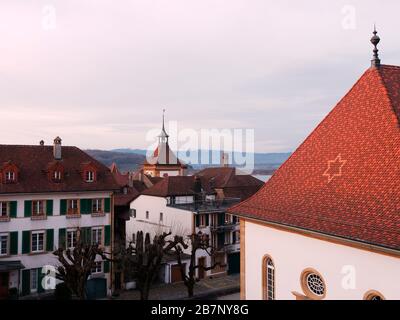 Blick auf die Altstadt von Murten oder Morat in der Schweiz in der Abenddämmerung. Das Dach der deutschen Kirche, der Glockenturm des Berner Tores und die Schweizer Alpen sind zu sehen. Stockfoto