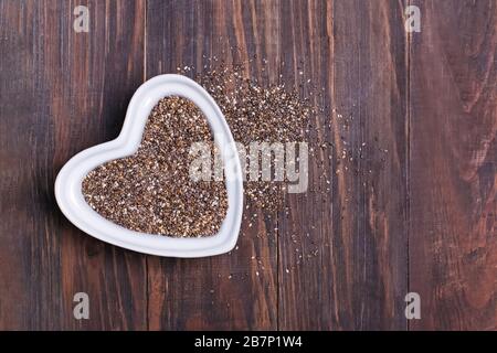Chia Samen in einer weißen, herzförmigen Schüssel auf Holzhintergrund. Salvia hispanica Samen. Stockfoto