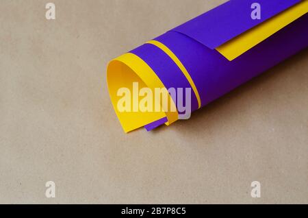 Nahaufnahme von blau und gelb gerollten Papieren vor beigefarbenem Hintergrund. Zwei Blatt farbiges Papier in einen Zylinder gefaltet. Abstrakter Hintergrund. Top VI Stockfoto