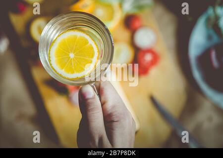 Eine nicht erkennbare Frau, die ein Glas Süßwasser mit einer Zitronenscheibe hält. Ernährungskonzept, organisches und gesundes Lebensmittelkonzept. Ansicht von oben. Stockfoto