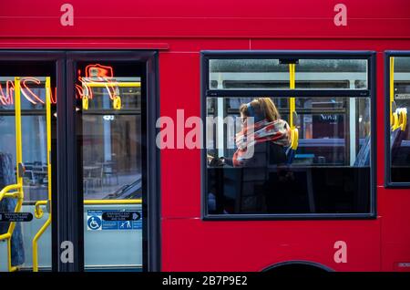 Ein einziger weiblicher Passagier sitzt und hört Musik mit Kopfhörern in einem roten Londoner Bus. Stockfoto