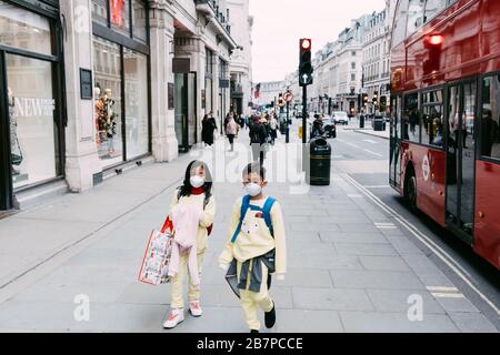 Zwei Kinder gehen auf einer ungewöhnlich ruhigen Regent's Street, London, Großbritannien, die während der Corona-Viruspandemik Gesichtsmasken trägt. märz 2020. Stockfoto