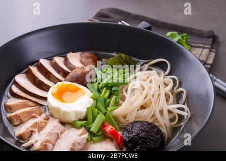 Japanische Rammsuppe mit Huhn, Pilzen, Pasta, Ei und Schnittlauch auf schwarzem Grund Stockfoto