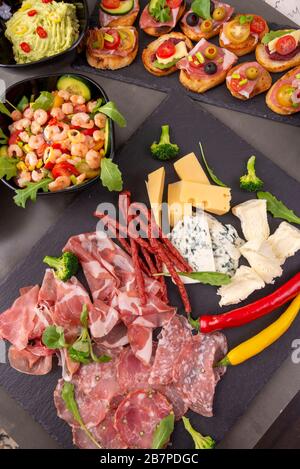 Verschiedene Vorspeisen auf einem Schieferteller. Schinken, Käsewurst und Guacamole. Ansicht von oben Stockfoto