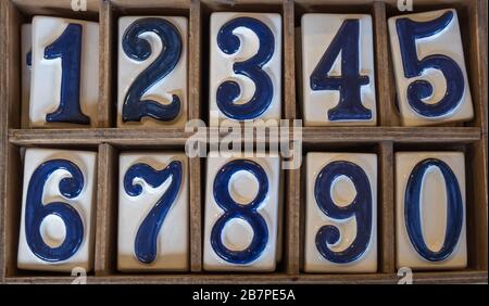 Blau-weiße Keramikfliesen mit den erhöhten Zahlen 0 bis 9, die in zwei Reihen in Holzkiste angeordnet sind. Stockfoto