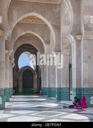 Casablanca, Marokko: Menschen in traditioneller Kleidung, die auf dem Boden unter Bögen der Hassan-Moschee sitzen Stockfoto