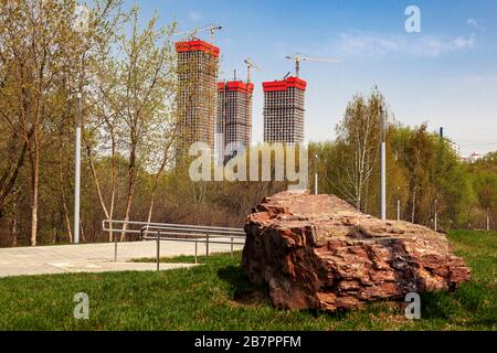 Drei Hochhäuser werden vor blauem Himmel gebaut. Im Vordergrund steht ein großer Granitstein Stockfoto