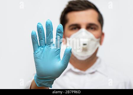 Porträt des Arztes in medizinischer Uniform mit einer schützenden Gesichtsmaske und einer Handschuhhand, die ein Stoppschild zeigt. COVID-19-Konzept beenden. Stockfoto