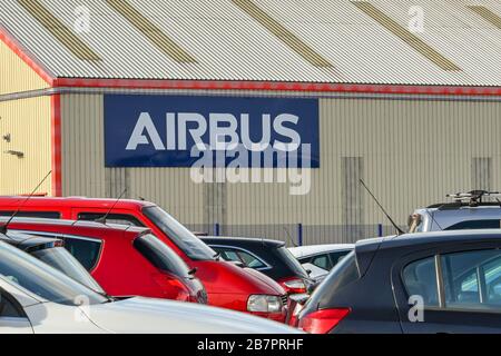 BROUGHTON, WALES - MÄRZ 2020: Schild an der Seite eines Fabrikgebäudes im Airbus-Werk in Broughton, wobei die Autos der Mitarbeiter im Vordergrund stehen. Stockfoto