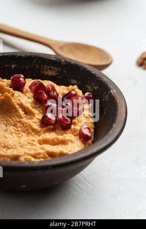 Gesunder Snack, Gourmet-Bad. Hummus mit geröstetem Paprika und Granatapfelsamen oben in Keramikschale, Nahaufnahme Stockfoto