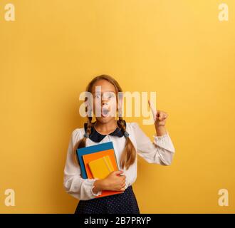 Der junge Student ist schockiert und zeigt etwas an. Gelber Hintergrund Stockfoto