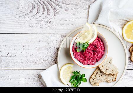 Beetwurzelhummus mit Meerrettich und Zitronensaft, serviert auf Platte mit frischen Petersilienkräutern und Vollkornbrot auf rustikalem Holztisch, Pflanzen Stockfoto