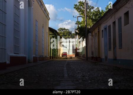 Ein rotes Klassik-Auto, das am späten Nachmittag in Trinidad (Kuba) bei Sonneneinstrahlung angezündet wird, während die Straße davor in Schatten fällt. Gefangen genommen am 27. November 2 Stockfoto