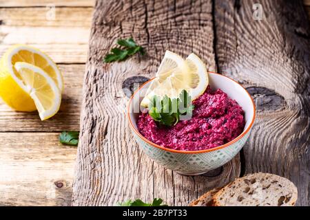 Beetwurzelhummus mit Meerrettich und Zitronensaft, serviert auf Platte mit frischen Petersilienkräutern und Vollkornbrot auf rustikalem Holztisch, Pflanzen Stockfoto