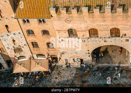 San Gimignano, Toskana / Italien: Blick auf die beliebte und geschäftige Piazza del Duomo und den Palazzo Vecchio del Podestà vom Gipfel des Torre Grossa. Stockfoto
