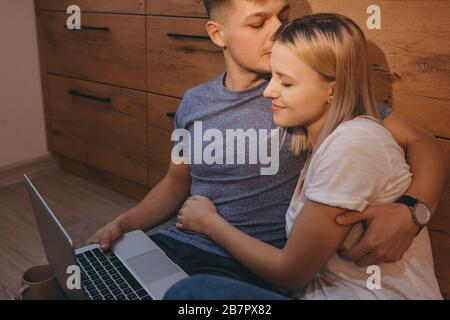 Vorsichtiger kaukasischer Mann küsst seine blonde Frau, während er mit einem Laptop einen Tee zusammen hat Stockfoto