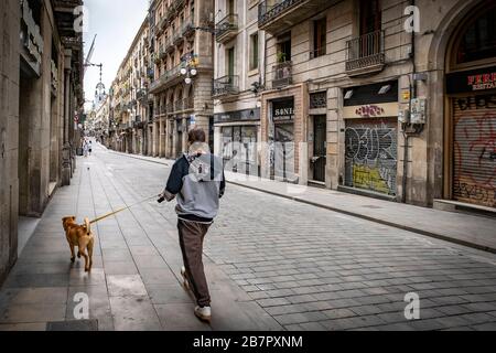 Während der Corona-Virus-Pandemie spaziert ein Mensch seinen Hund durch eine halbverlassene Straße.die Bewohner von Barcelona stehen am dritten Tag der Hauseinschließung mit den Straßen, die aufgrund der Bedrohung durch das Coronavirus fast leer sind. Stockfoto