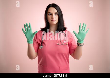 Das Porträt eines schönen Frauenarztes mit Stethoskop mit rosafarbenen Schruben zeigt beide Hände mit medizinischen Handschuhen, die auf einem rosafarbenen, isolierten Hinterteil posieren. Stockfoto