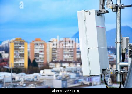 5G neue Funk-Telekommunikationsnetzantenne auf einem Metallpol, die starke Signalwellen von der Dachspitze in der Großstadt liefert Stockfoto