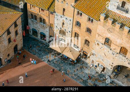 San Gimignano, Toskana / Italien: Blick auf die beliebte und geschäftige Piazza del Duomo und den Palazzo Vecchio del Podestà vom Gipfel des Torre Grossa. Stockfoto