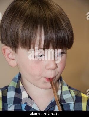 Kleiner Junge mit blauen Augen, der ein alkoholfreies Getränk aus einem Strohhalm trinkt, der zufrieden aussieht. Stockfoto