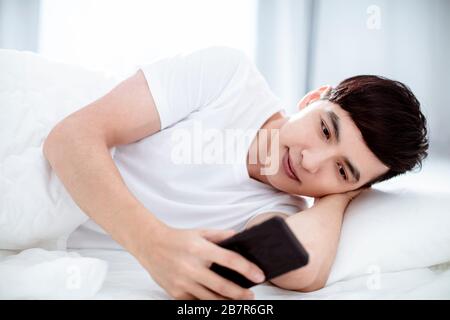 Gutaussehender junger Mann, der Handy im Bett beobachtet Stockfoto