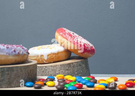 Süße Feriendonuts auf Holzwald stehen mehrfarbige Schokoladen kleine Süßigkeiten auf grauem Hintergrund Nahaufnahme. Stockfoto