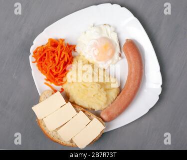 Herzhaftes köstliches Mittagessen. Geröstete Eierwurst und Kartoffel mit einem kitschigen Sandwich auf einem weißen Teller. Grauer Hintergrund Nahansicht oben. Stockfoto