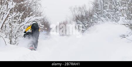 Ein Athlet reitet, treibt auf einem Schneemobile auf einer schneebedeckten Straße vor dem Hintergrund einer Winterwaldlandschaft Stockfoto