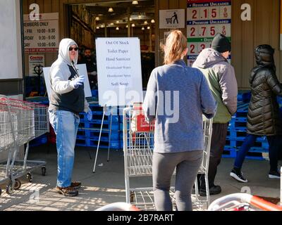 Melrose Park, Illinois, USA. März 2020. Käufer betreten das Costco Lagerhaus in diesem westlichen Vorort von Chicago während der COVID-19-Pandemie. Ein Schild weist darauf hin, dass der Store aufgrund eines Panikkaufs nicht mehr von mehreren Hygieneprodukten entfernt ist, da ein Mitarbeiter die Leute anweist, das Schild zu lesen. Stockfoto