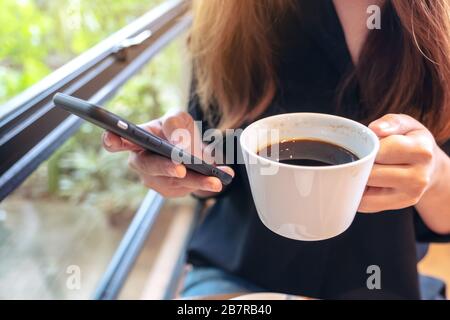Nahaufnahme einer Frau, die beim Kaffeetrinken ein Smartphone hält, verwendet und berührt Stockfoto