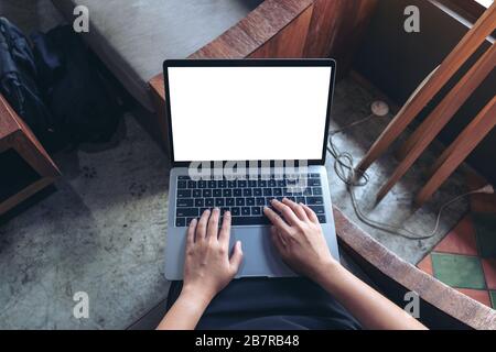 Top-View-Mockup-Bild von Geschäftsfrau, die auf dem Laptop mit leerem weißem Desktop-Bildschirm während des Sitzens im Café verwendet und tippt Stockfoto