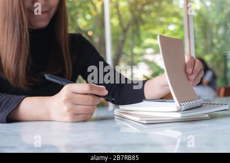 Nahaufnahme einer Geschäftsfrau, die ein leeres Notizbuch hält und öffnet, um auf einen Tisch mit grünem Hintergrund zu schreiben Stockfoto