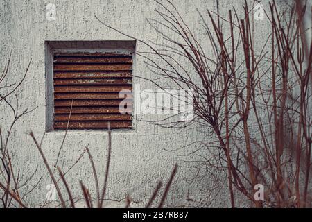 Verrostete kleine Lüftungsfenster an der grauen Wand Stockfoto