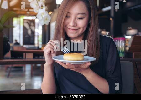 Eine schöne asiatische Frau, die eine Gabel hält, um ein Stück Donut zu schneiden und sich im Café glücklich zu fühlen Stockfoto