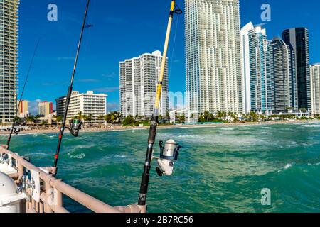 Drei Angelruten an einem Pier mit Hochhäusern in der Ferne, Florida. Stockfoto