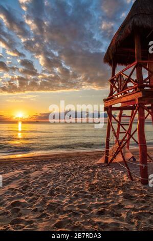 Sonnenaufgang über den tropischen Stränden der Riviera Maya in der Nähe von Cancun, Mexiko, mit Rettungsschwimmturm mit Blick auf das karibische Meer. Vertikale Ausrichtung. Stockfoto