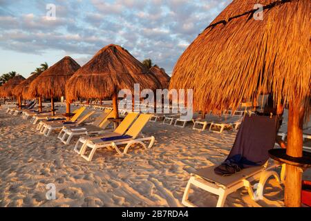 Sonnenaufgang über Lounge-Sesseln und Sonnenschirmen an einem karibischen Strandurlaub an der Riviera Maya in Cancun, Mexiko. Stockfoto