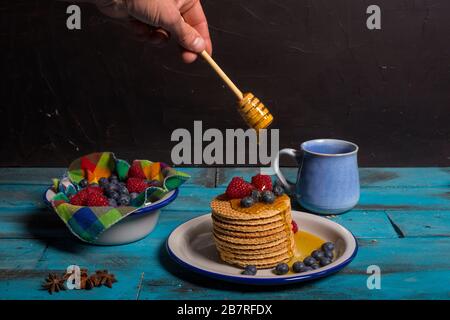 Geben Sie Honey mit Honeydewöffel über Waffeln mit Blaubeeren und Himbeeren zum Frühstück auf blauem Holzhintergrund. Frühstückskonzept Stockfoto