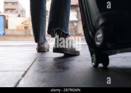 Nahaufnahme der Füße einer Frau während der Reise und ziehen eines schwarzen Gepäckstücks im Freien Stockfoto