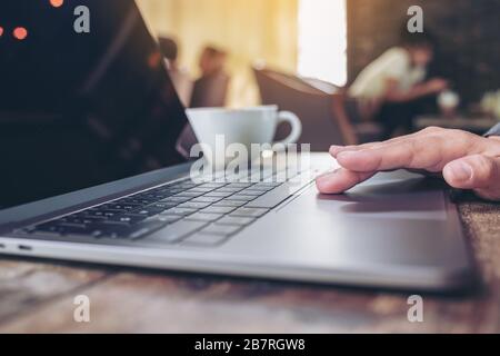 Nahaufnahme der Hand mit und Berühren des Touchpads auf dem Laptop mit Kaffeetasse auf Holztisch im Café Stockfoto