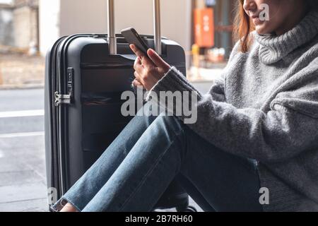 Nahaufnahme einer Frau, die mit einem schwarzen Gepäck auf dem Handy sitzt und es verwendet, um zu reisen Stockfoto
